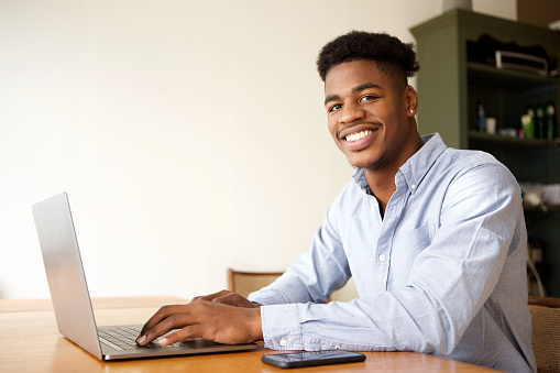 Portrait of charming young african american man working with laptop computer at office